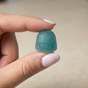 A hand with pale pink nails holds a single Kuli Kuli Foods Sea Moss & Blue Spirulina Superfood Gummy between the thumb and index finger against a neutral background.