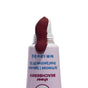 A close-up of an open tube of The Seaweed Bath Co Tinted Mineral Lip Shine SPF 20, with a deep berry-tinted balm emerging over the white applicator tip. Enriched with shea butter and organic Atlantic seaweed, the light pink tube features blue text.