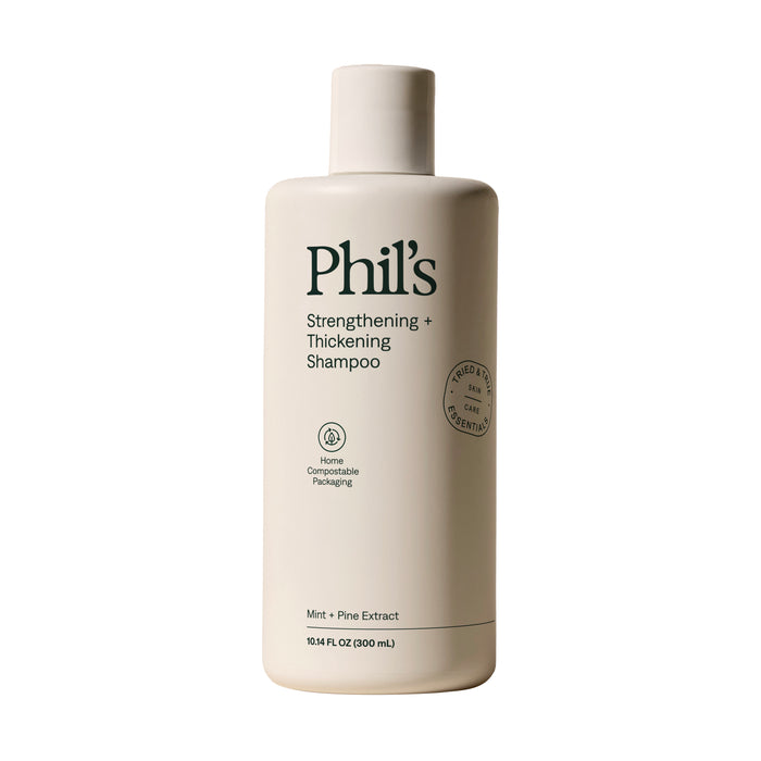 A 10.5 fl oz (300 mL) white bottle of Phil’s Strengthening + Thickening Shampoo with green text, featuring mint and pine extracts for scalp health in home compostable packaging.