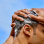 A close-up of a person washing short hair with Phil's Strengthening + Thickening Shampoo, creating rich lather for scalp health, set against a bright blue sky.