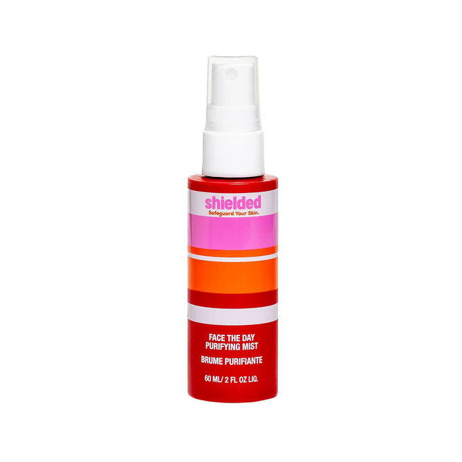A red, orange, and pink striped spray bottle of Shielded Beauty Face the Day Purifying Mist (60 mL/2 fl oz) is shown on a white background. This facial spray delivers antioxidant protection for healthier skin.