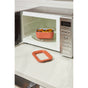 A Caraway Mini Food Storage Set W/ Storage container holds cooked food inside an open microwave oven on a white countertop, with its matching lid nearby—ideal for organized kitchens.