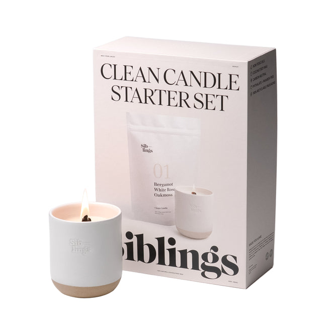 The Clean Candle Starter Set by Siblings includes a lit white candle in a minimalist Forever Vessel holder, beside a box labeled with the product name and featuring text and images of Siblings candles that describe their clean-burning properties and elevate your space with luxurious fragrance.