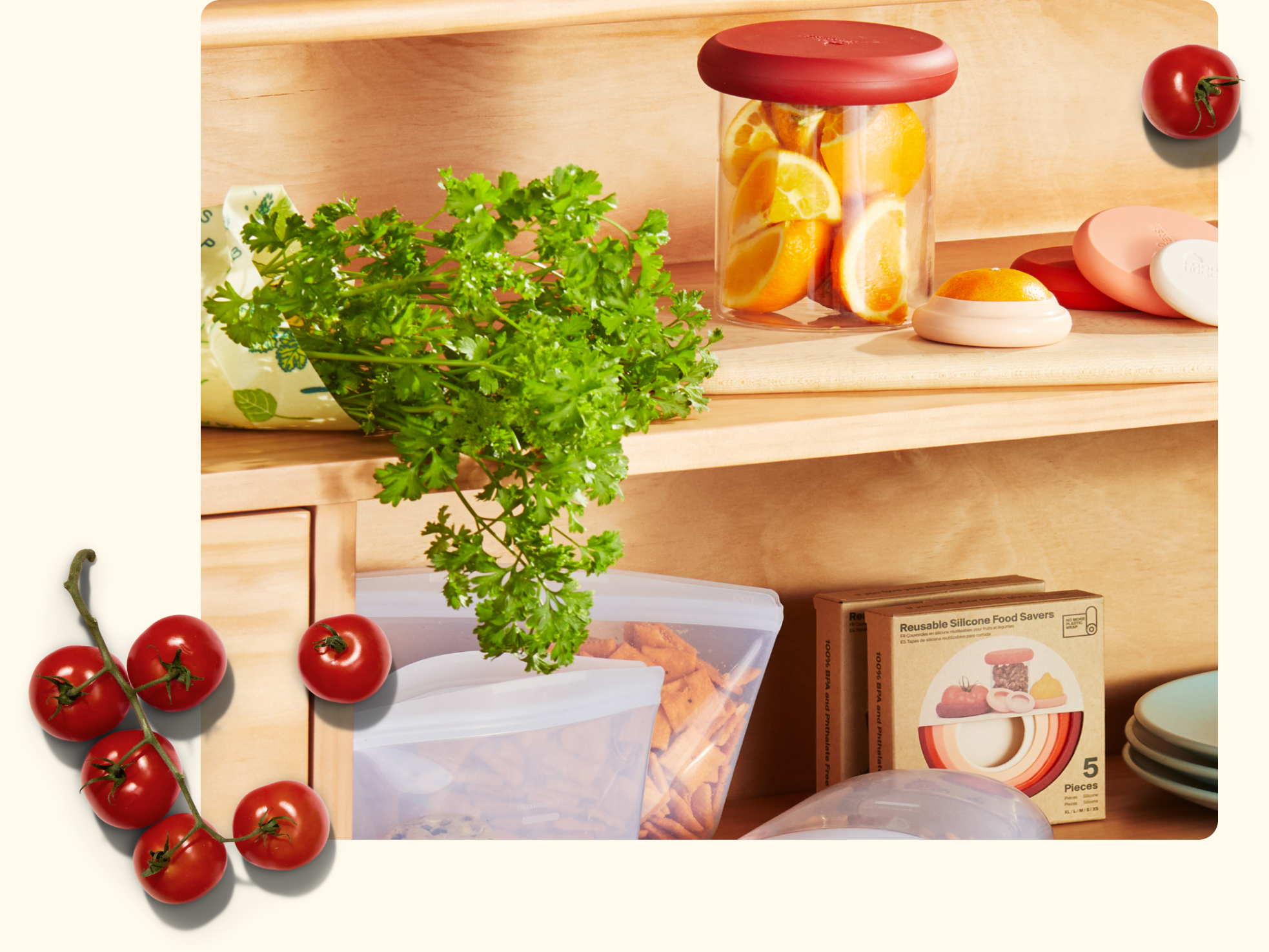 A wooden shelf holds a jar with orange slices, a bunch of fresh parsley, reusable silicone food bags with snacks, a box of food savers, and a cluster of tomatoes on the vine.