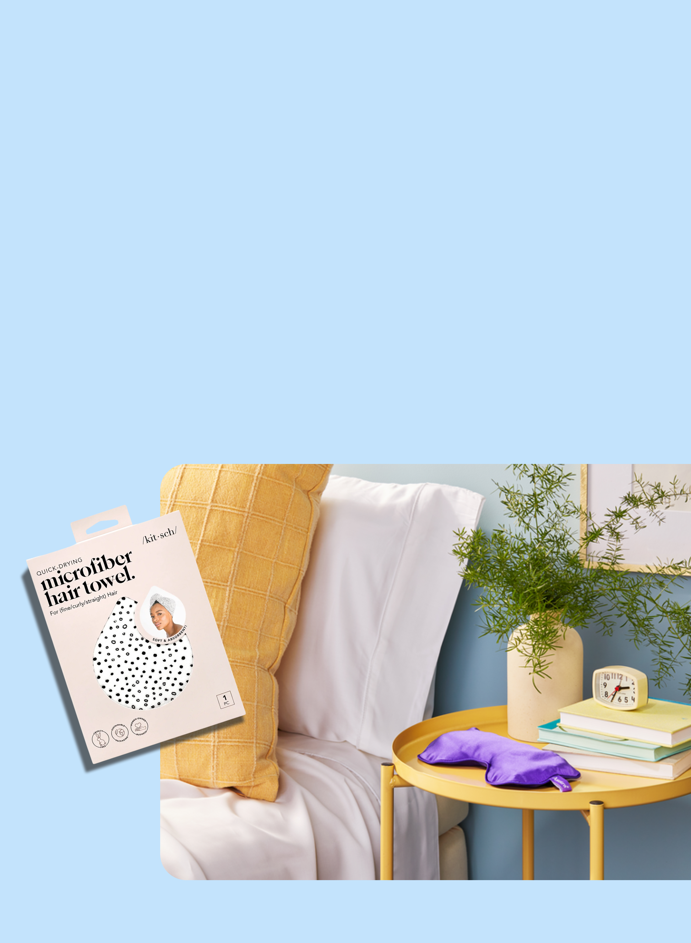 A cozy bedside scene with a bed, white and yellow pillows, a round yellow side table holding a purple hair towel, books, a clock, a vase with greenery, and a box labeled microfiber hair towel.