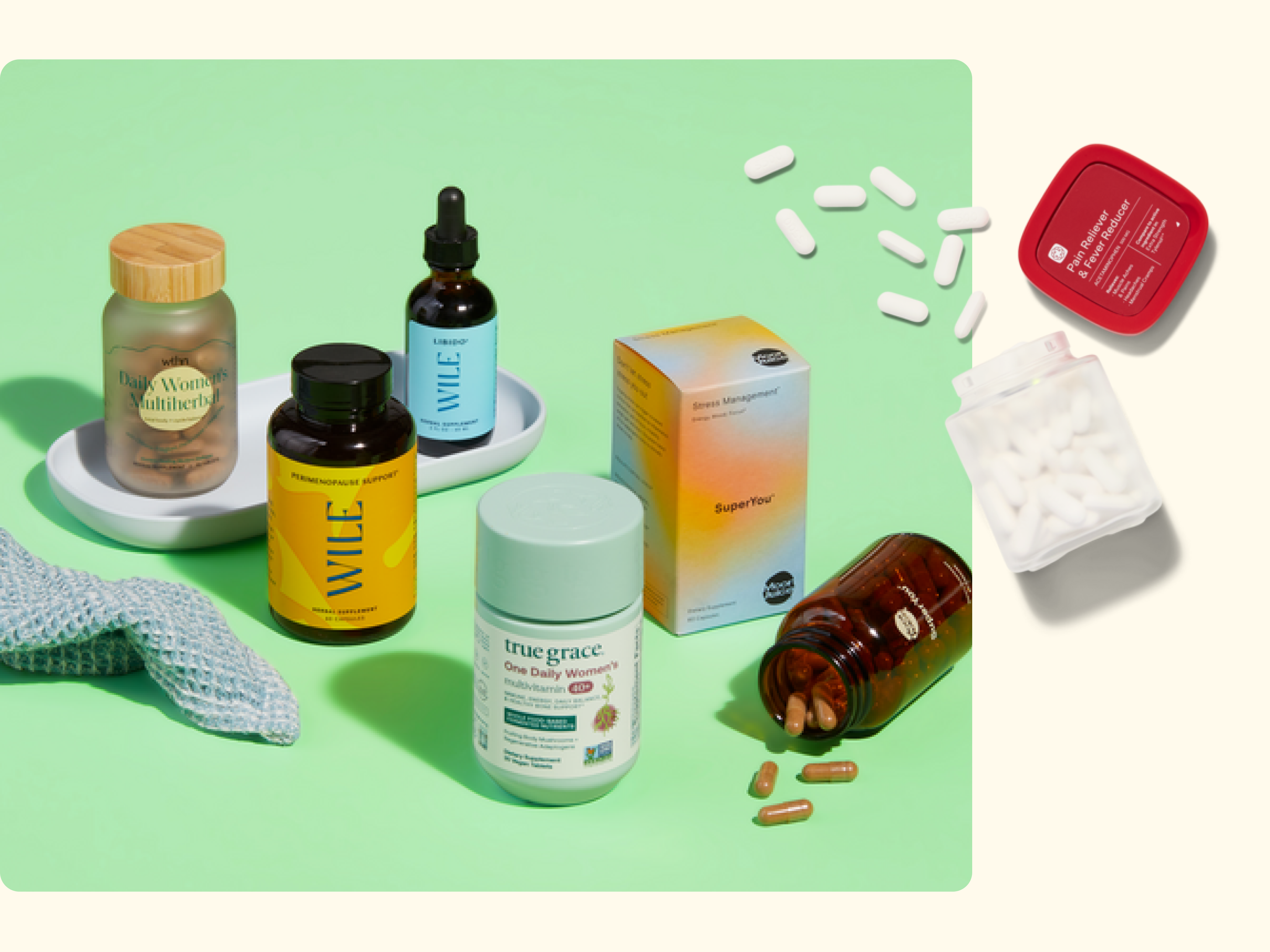 A variety of supplement bottles, pill containers, and capsules are arranged on a green surface with a blue cloth, a small tray, and scattered pills nearby. The background is light cream.