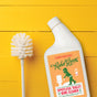 A Rebel Green Toilet Bowl Cleaner with an orange label and a white toilet brush sit on a bright yellow wooden surface.