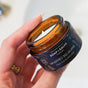 A hand holds an open amber jar labeled Chagrin Valley Soap & Salve Whipped Squalane Face & Eye Mousee, showing the creamy plant-based moisturizer inside.