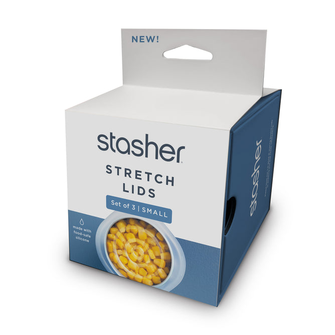 A blue and white box labeled Stasher Reusable Stretch Lids 3-pack Small shows a bowl of corn covered by a reusable lid. The packaging highlights food-safe silicone and airtight storage.