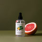 A Koala Eco Room Spray bottle, featuring a citrus fruit illustration on its label, stands beside a halved grapefruit against an olive-green background, evoking the invigorating scent of the Australian bush.