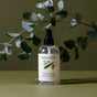 A bottle of Koala Eco Pillow & Linen Spray rests on a green surface, surrounded by eucalyptus leaves, evoking a fresh and natural ambiance.