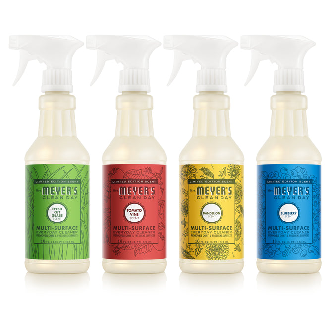 The Mrs. Meyer's Summer Multi-Surface Cleaner Collection includes four spray bottles in Fresh Grass, Tomato Vine, Dandelion, and Blueberry scents, each with unique decorative labels.