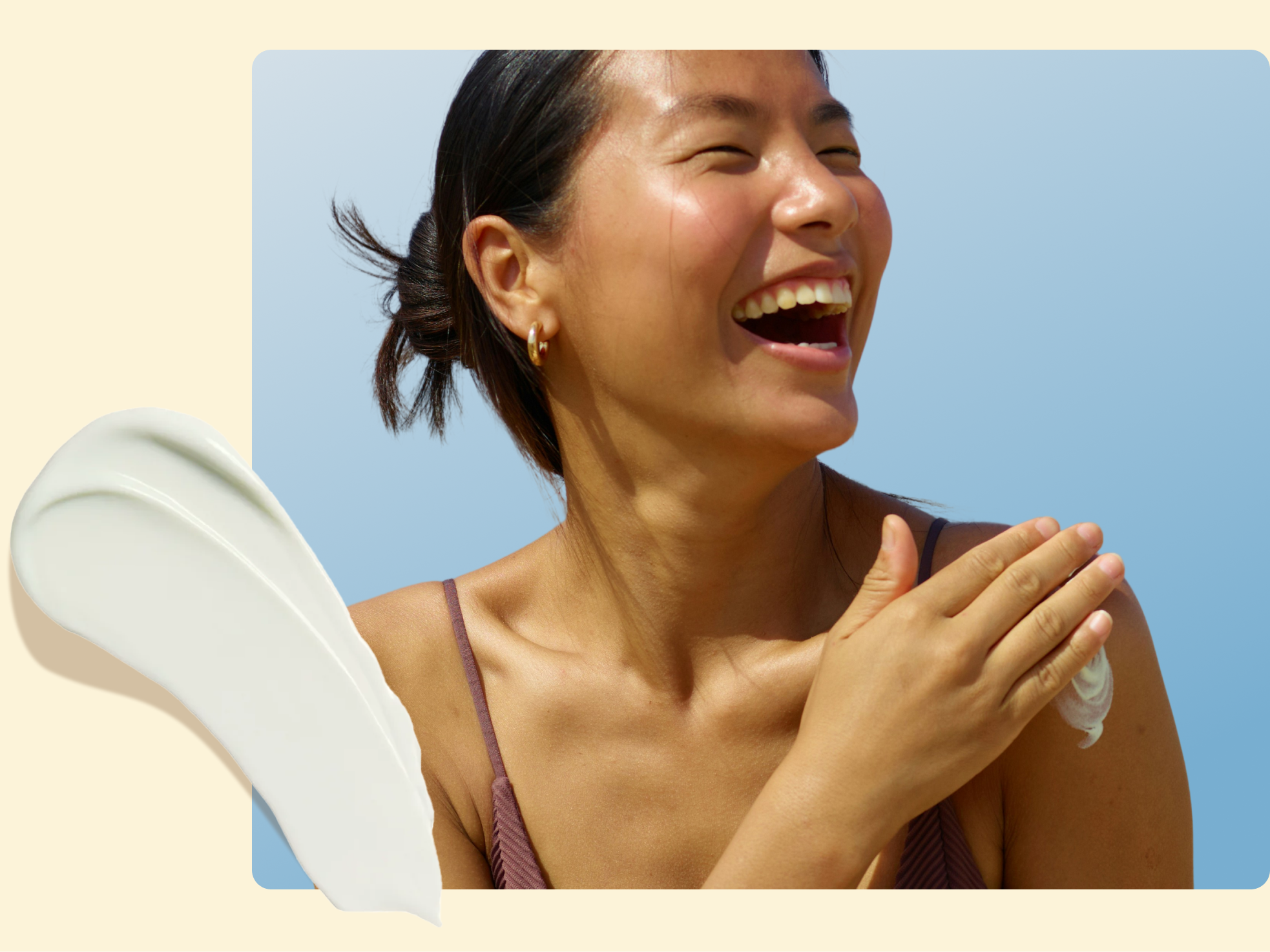 A woman smiling and applying lotion to her shoulder, with a smear of white cream shown on the left. She is wearing a brown camisole and gold hoop earrings against a blue and beige background.