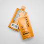 Two orange pouches of Acure Mineral Sunscreen SPF 50 ($7.99 value) are displayed on a white background—one shows the front with the brand name “Acure” and SPF 50, while the other reveals the ingredients and barcode.