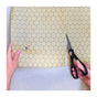 Someone uses black scissors to cut a SuperBee Beeswax Wrap Roll—yellow with a hexagonal pattern—as reusable food wrap, steadying the material with one hand.