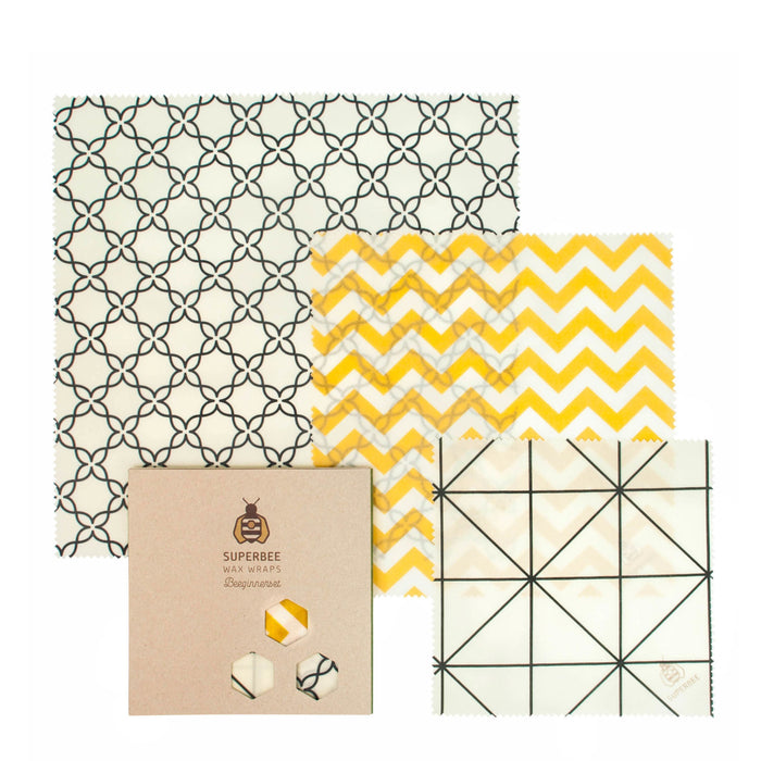 The SuperBee Beeswax Wrap Beeginner Set includes three reusable wraps in black geometric, yellow zigzag, and black grid patterns, plus brown packaging featuring the SuperBee logo and food wrap illustrations.