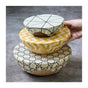 A hand holds the middle of three wooden bowls, each topped with SuperBee’s Beeswax Wrap Beeginner Set—plastic-free, reusable wraps in geometric patterns—demonstrating an eco-friendly food storage solution on a gray surface.