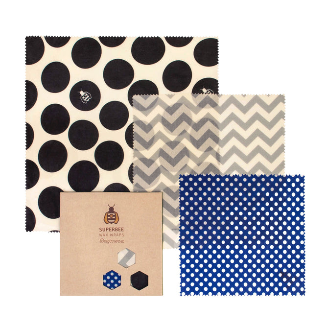 The SuperBee Beeswax Wrap Beeginner Set features three reusable food wraps in black polka dots, grey zigzag, and white polka dots on blue, displayed next to a brown SuperBee box for eco-friendly food storage.