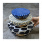 Three bowls covered with SuperBee Beeswax Wrap Beeginner Set in assorted patterns; a hand holds the largest bowl, showcasing eco-friendly food storage.