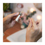Close-up of hands pulling Dentos Eco Dental Floss by SuperBee from a small glass container, with a blurred bathroom background. This plastic-free floss is an eco-friendly choice for your oral care routine.