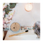 A bamboo toothbrush, SuperBee Dentos Eco Dental Floss, and a tin of toothpaste tabs rest on a bathroom sink beside a plant and soap dispenser, with tiled walls and warm lighting creating a plastic-free routine vibe.