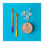 Two bamboo toothbrushes with purple and yellow handles, a tin of SuperBee Dentos Eco Toothpaste Tabs (Spearmint), and scattered vegan tabs are displayed on a bright blue background for a travel-friendly toothpaste solution.