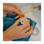 A person holding a SuperBee Dentos Eco Toothpaste Tabs container (Spearmint Flavor) and a bamboo toothbrush above a sink, with a blue cloth in their hands.