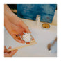 A person holds SuperBee Dentos Eco Toothpaste Tabs (Spearmint) in one hand and a bamboo toothbrush in the other, above a bathroom sink with a blue pouch—highlighting this travel-friendly toothpaste solution.