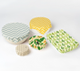 SuperBee Essentials Beeswax Wraps—set of 5 in assorted sizes and vibrant patterns (zigzags, avocados, honeycomb, abstract shapes)—cover bowls and a dish, providing a colorful plastic-free food storage solution against a white background.