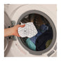 A hand holds a small white mesh laundry bag in front of an open washer, ready to pair with SuperBee’s Hexawash Laundry Detergent Substitute for a safer, fresher clean.