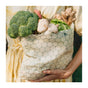 A person in a yellow dress holds a SuperBee Waxed Food Bag filled with fresh vegetables such as broccoli, lettuce, mushrooms, and ginger.