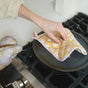 Someone lifts the lid off a pan on a gas stove in the kitchen using the Supra Endura Hand Block Printed Ovenmitt And Pot Holder Set.