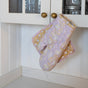 A Supra Endura Hand Block Printed Ovenmitt And Pot Holder Set hangs on a brass cabinet knob in a white kitchen with paneled walls and glass-front cabinets.