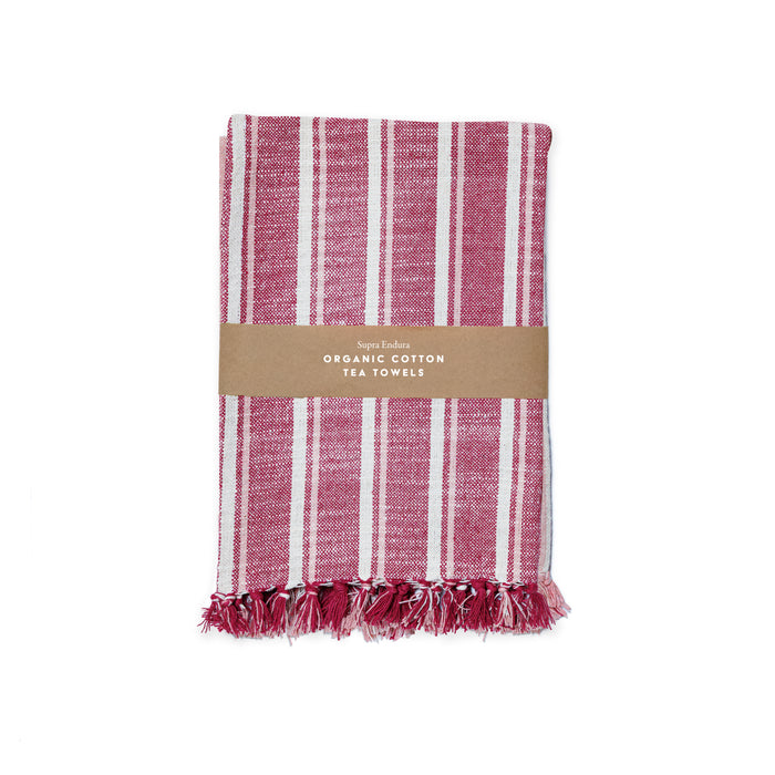 A folded red and white striped organic cotton tea towel with fringed edges, wrapped in a brown paper band labeled Supra Endura Striped Organic Cotton Tea Towel Set.