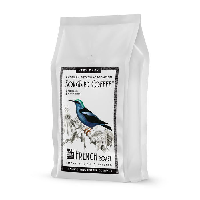 A white Songbird Coffee bag by Thanksgiving Coffee shows a vibrant bird design and florals. The text reads Very Dark, French Roast, Smoky, Rich, Intense. This Bird Friendly Coffee features the American Birding Association logo—symbolizing sustainable excellence.