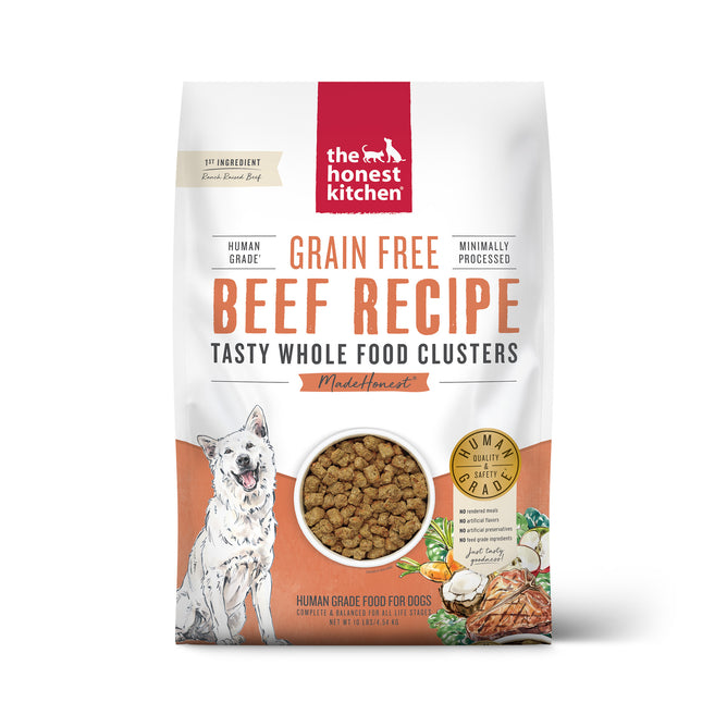 A white bag of The Honest Kitchen Dry Dog Food, Grain Free Beef Whole Food Clusters, features a dog illustration, a clear window with whole food clusters, and images of beef and vegetables at the bottom right.