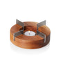 The AdHoc Borosilicate Glass Teapot with Stainless Steel Infuser sits atop a round acacia wood base with four metal supports in a cross shape, holding a tealight candle at the center for gentle warming.