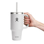 A hand holds a sleek white 32 oz Hydro Flask Travel Tumbler with double-wall vacuum insulation, a silver leak-resistant lid and straw. The iconic Hydro Flask logo adorns its travel-friendly design.