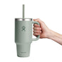 A hand holds a 32 oz sage green Hydro Flask Travel Tumbler with a large handle and straw, designed with double-wall vacuum insulation for perfect temperature maintenance. It features the Hydro Flask logo and sleek metal rim, combining functionality with elegance.