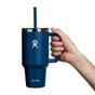 A hand holds a 32 oz Hydro Flask Travel Tumbler, featuring a blue color, lid, straw, white logo, and large handle against a white background. Its double-wall vacuum insulation maintains drink temperature perfectly.