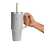 A hand holds a 40 oz gray Hydro Flask Travel Tumbler with a straw. Its sleek design includes a handle and logo, offering double-wall vacuum insulation to maintain your drinks optimal temperature on the go.