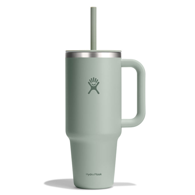The sage green 40 oz Hydro Flask Travel Tumbler has a large handle, leak-resistant lid with straw access, and double-wall vacuum insulation to keep drinks at temperature. It features an embossed logo of a person with raised arms above the brand name.