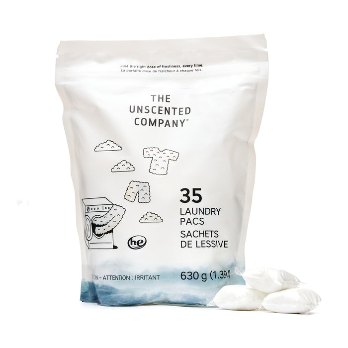 A white bag of The Unscented Company Laundry Detergent Pacs stands upright with three white pacs nearby. The recyclable packaging features simple laundry and washing machine illustrations.
