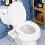 A white toilet fitted with the TUSHY Classic 3.0 Bidet Attachment, which has a self-cleaning nozzle and wooden knob for water pressure, sits against a blue tiled wall. To the right is a shelving unit holding towels and baskets.