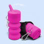 Two bright pink TUSHY Travel Portable Bidets with carabiner clips—one expanded upright, the other folded in a black pouch—sit against a light blue background.
