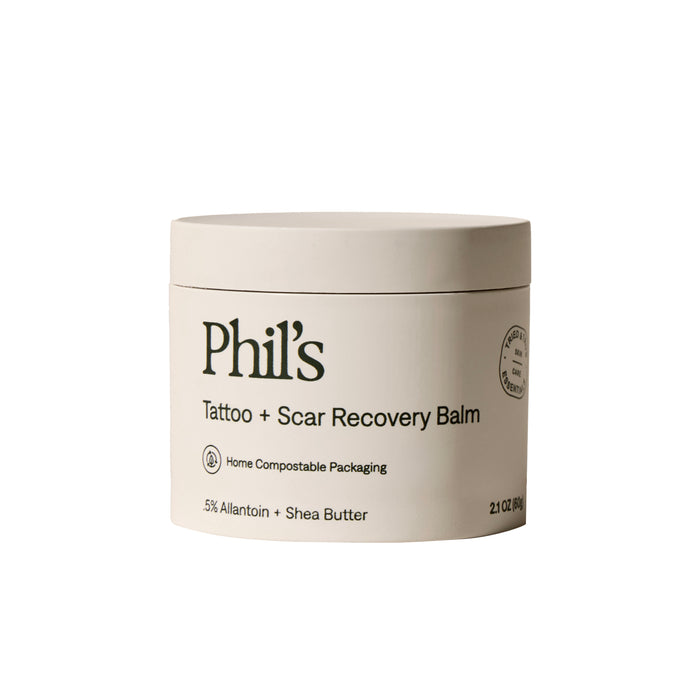 A 2 fl oz (60g) beige container of Phil's Tattoo + Scar Recovery Balm, featuring tattoo aftercare info, home compostable packaging, and highlights of 5% allantoin and shea butter on the label.