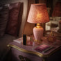 A pink bedside table with ornate gold accents holds a patterned pink lamp, perfume bottles, a small book, and Terra Intimacy Wipes—Daily pH Balancing, fragrance & sulfate free, individually wrapped—creating a cozy, elegant vibe.
