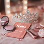 A sparkling tiara sits behind a pink Terra Micellar Water Facial and Makeup Removing Wipes packet infused with Aloe & Vitamin E, surrounded by a blush compact, lipstick, pearls, and pink roses on an elegant vanity.