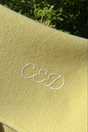 The Sawa - Citron pale yellow, plant-dyed merino baby blanket embroidered with the letters CeD in white cursive.