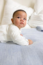 A baby in a white shirt lying on their stomach on a textured Sky Blue The Sawa merino baby blanket.